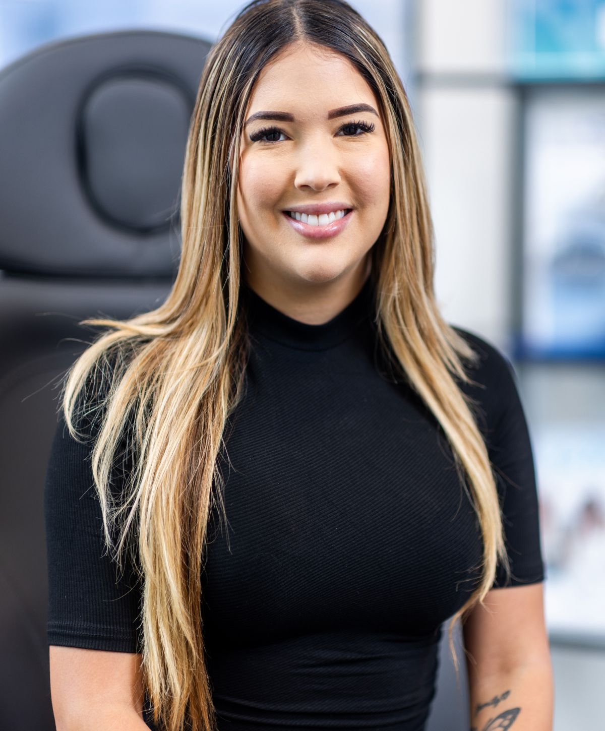 Smiling woman in black shirt, seated against backdrop.